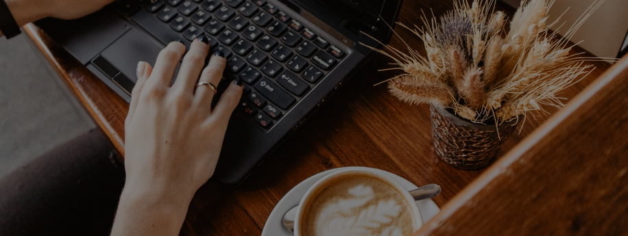 hands on black laptop with latte on desk_cropped