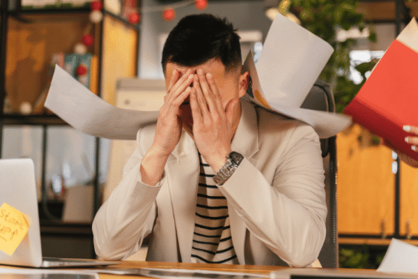 overwhelmed by marketing focus on this_featured image man sitting at desk with hands covering eyes surrounded by scattered papers relating to overwhelm as a solopreneur