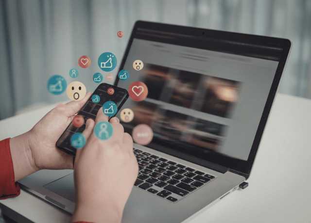woman holding cell phone at laptop relating to marketing analytics